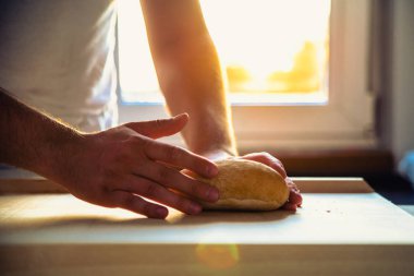 Adam, aşçı bir ekmek rulo elinde, ekmek üstünde belgili tanımlık sayaç tutar. Adam ekmek mutfakta batan güneşin arka planı elinde tutuyor.