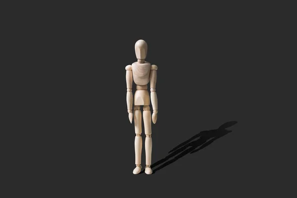 Wooden mannequin in a standing pose. Wooden model with lowered hands, isolated on a dark gray background.