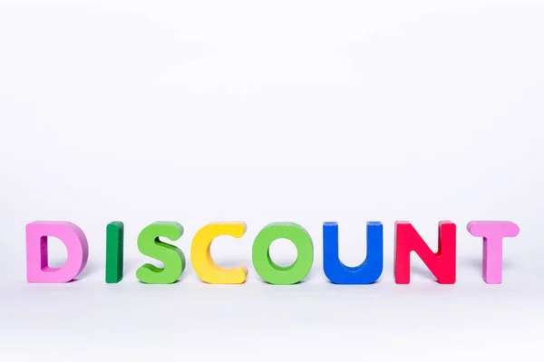 Word DISCOUNT on an isolated white background. DISCOUNT message made up of wooden and colorful letters with scattered letters. Discount concept in the store.