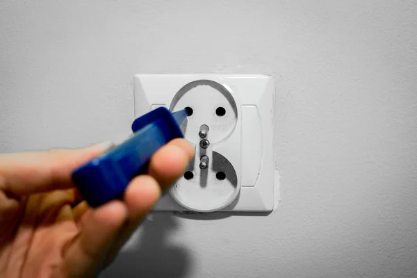 Blue screwdriver in an electric socket. The electrician checks if the current flows in the socket using a screwdriver with a current flow meter.