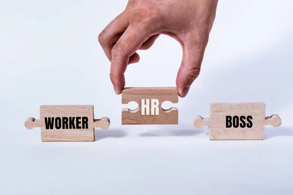 Hand holding a wooden jigsaw puzzle with HR word and worker, boss. There is a matching puzzle next to it. The concept Human resources concept, HR connects the employee with the employer.