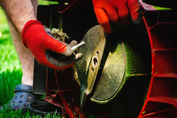 Man exchanges the mower\'s knife with a new one. Mowing the grass. Gardener mows the grass with a red electric mower. Work in the garden, spring cleaning. Care for the garden and grass.