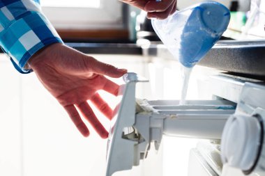 Çamaşırhane yapıyor. Çamaşır tozu çamaşır makinesi koyarak. Adam çamaşır makinesinde çamaşır yapar. Giysi temizliği. Bir adam bir kadının rolü olağandışı rolü. 