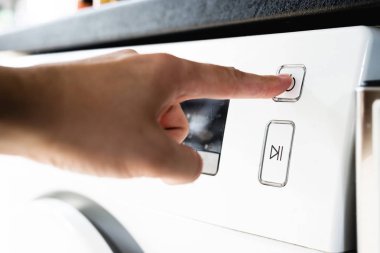 Çamaşırhane yapıyor. Adam çamaşır makinesi başlangıcı basar. Adam çamaşır makinesinde çamaşır yapar. Giysi temizliği. Bir adam bir kadının rolü olağandışı rolü. 