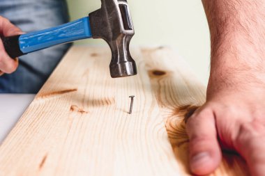 Ahşap plaka çivi çekiç. Tadilat, ev kavramı. Adam mavi çekiç çivi diğer elinde tutan, elinde tutuyor. Tamirci, DIY.