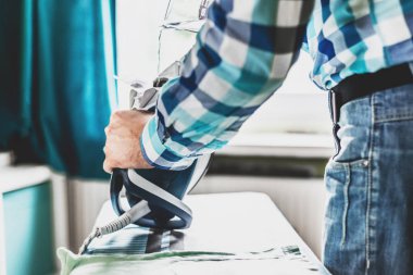 Adam evde elbise Ütü. Baba eve görevleri gerçekleştirir, çocuğun giysileri Irons. Bir adam bir kadının evde rolü. Adam Ütü forması ile mavi demir buharlı ütü masası.