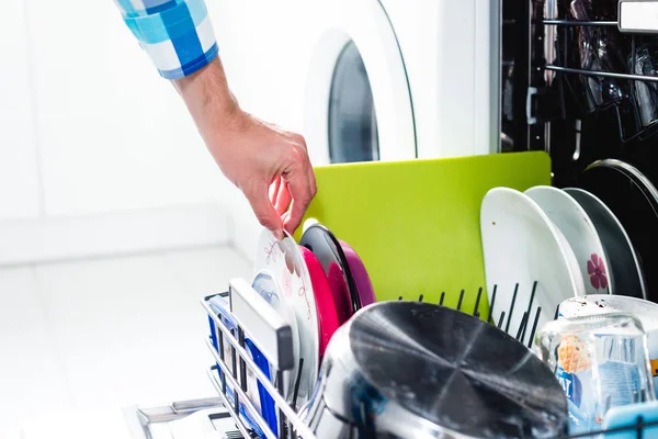 Washing dishes in the dishwasher. The man puts dirty dishes in the dishwasher. Opening and closing the dishwasher. The man cares about the house, does his homework.