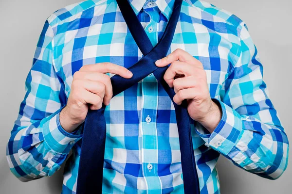 Putting on and tying a tie. The man is holding a tie. Instructions for putting on a tie. Preparation for the windsor node. Front view of a man in a blue shirt.