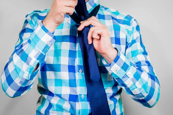 Putting on and tying a tie. The man is holding a tie. Instructions for putting on a tie. Preparation for the windsor node. Front view of a man in a blue shirt.