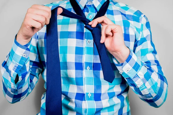 Putting on and tying a tie. The man is holding a tie. Instructions for putting on a tie. Preparation for the windsor node. Front view of a man in a blue shirt.