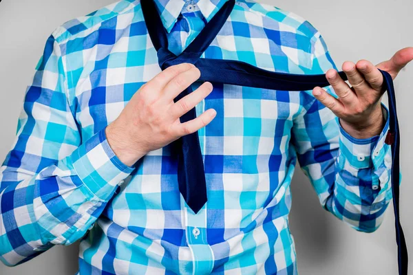 Putting on and tying a tie. The man is holding a tie. Instructions for putting on a tie. Preparation for the windsor node. Front view of a man in a blue shirt.