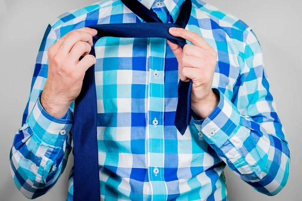 Putting on and tying a tie. The man is holding a tie. Instructions for putting on a tie. Preparation for the windsor node. Front view of a man in a blue shirt.