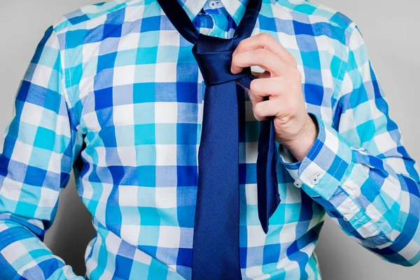 Putting on and tying a tie. The man is holding a tie. Instructions for putting on a tie. Preparation for the windsor node. Front view of a man in a blue shirt.