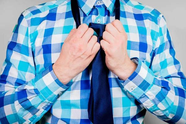 Putting on and tying a tie. The man is holding a tie. Instructions for putting on a tie. Preparation for the windsor node. Front view of a man in a blue shirt.