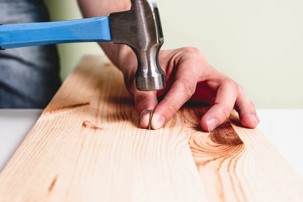 stock image Hammering a nail into wooden plate. Concept of renovation, housework. The man is holding a blue hammer in his hand, holding a nail in the other hand. Handyman, DIY.