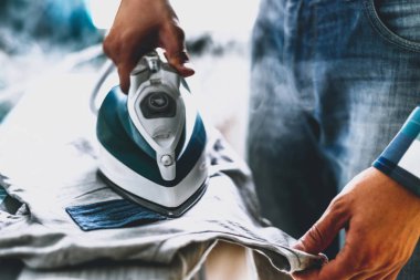 Adam evde elbise Ütü. Baba eve görevleri gerçekleştirir, çocuğun giysileri Irons. Bir adam bir kadının evde rolü. Adam Ütü forması ile mavi demir buharlı ütü masası.