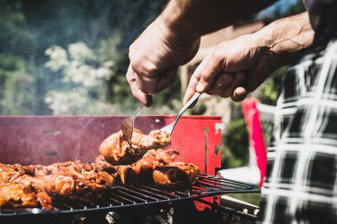 Tavuk ızgara çekerek. Adam bitmiş tavuk budu ızgarada çeker. Grill'de aile ile birlikte vakit. Sosyal toplantılar, arkadaşlar. Odun ve kömür ile kırmızı kiremit.