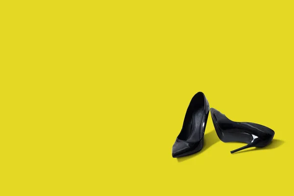 Black high heels isolated on a yellow pastel background. Fashion concept, catwalk. Modern online store, fashion store, shoe sales store. The high heel lies next to the other.