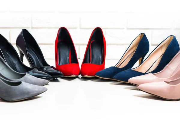 Red high heels. Female high heels shoes are standing on the floor, a wall of light brick, next to the wall. Bright floor, bright colors. Five pairs of footwear. Authentic shoes, lifestyle.