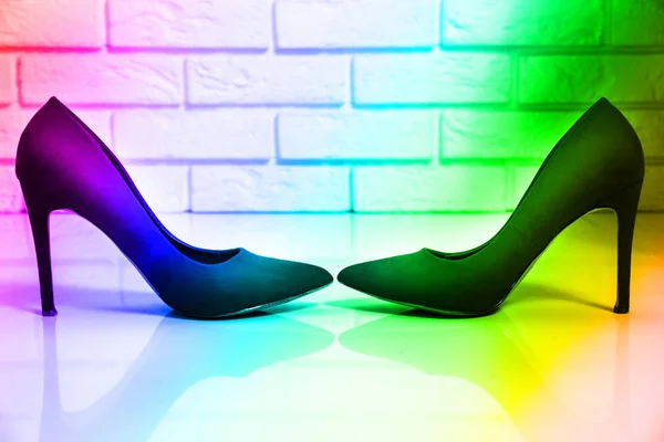 Colorful high heels. Two women's high heels shoes are standing on a bright floor, a white brick wall facing each other. Rainbow, bright colors.