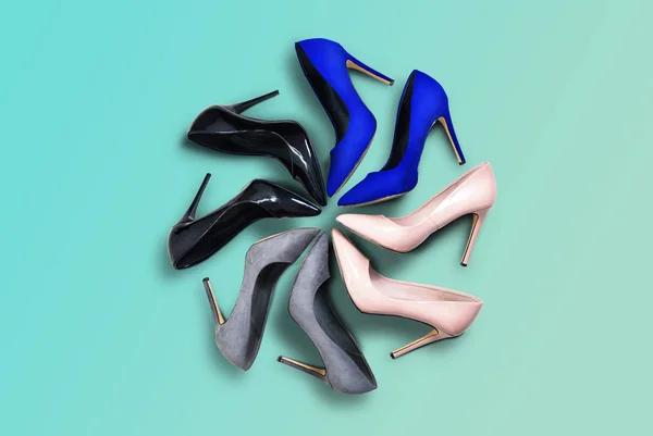 High heels. Top view of different colors of high heels isolated green pastel background. High heels arranged in a circle. Matt and shiny high heels. Fashion and beauty concept. Footwear for women.
