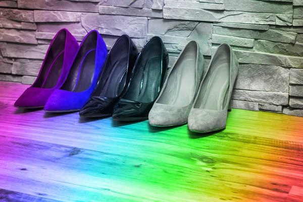 Colorful high heels. Female high heels shoes are standing on the floor, a dark brick wall by the wall. Rainbow, bright colors. Three pairs of footwear.