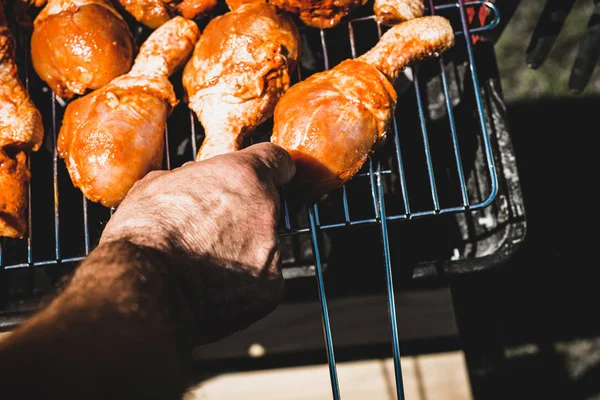 Laying the chicken on the grill. The man puts chicken legs on the grill. Spending time together with the family at the grill. Social meetings, friends. Red gril with kindling and coal.