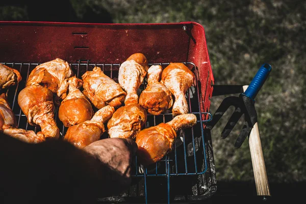 Laying the chicken on the grill. The man puts chicken legs on the grill. Spending time together with the family at the grill. Social meetings, friends. Red gril with kindling and coal.