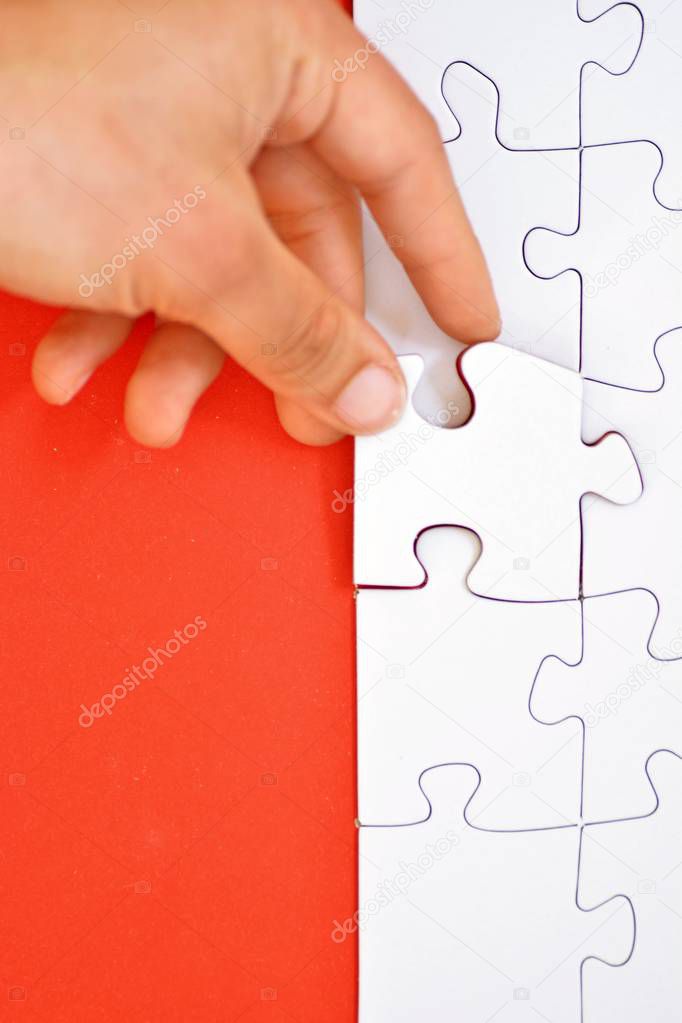 Hand put the last piece of a white puzzle to complete the mission