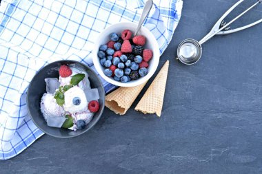Koyu bir mutfak yüzeyinde yanında nane yaprakları ve dondurma waffle ile yabani berry dondurma topları dolu koyu bir kase - yaz için ferahlatıcı meyve buz ile kavram