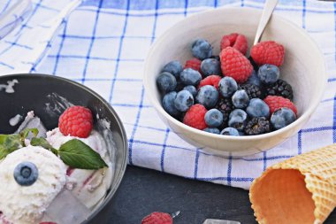 Koyu bir mutfak yüzeyinde yanında nane yaprakları ve dondurma waffle ile yabani berry dondurma topları dolu koyu bir kase - yaz için ferahlatıcı meyve buz ile kavram
