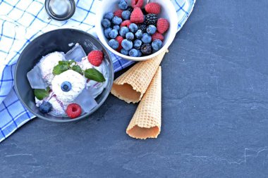 Koyu bir mutfak yüzeyinde yanında nane yaprakları ve dondurma waffle ile yabani berry dondurma topları dolu koyu bir kase - yaz için ferahlatıcı meyve buz ile kavram