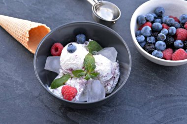 Koyu bir mutfak yüzeyinde yanında nane yaprakları ve dondurma waffle ile yabani berry dondurma topları dolu koyu bir kase - yaz için ferahlatıcı meyve buz ile kavram