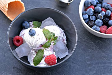 Koyu bir mutfak yüzeyinde yanında nane yaprakları ve dondurma waffle ile yabani berry dondurma topları dolu koyu bir kase - yaz için ferahlatıcı meyve buz ile kavram