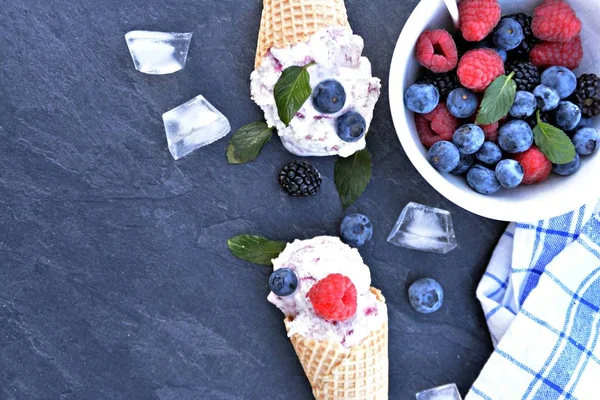 waffle ice cream cones filled with forest fruit ice cream balls with fresh berries and mint lying on a dark marble surface - concept for a cool summer adventure with delicious fruity ice cream