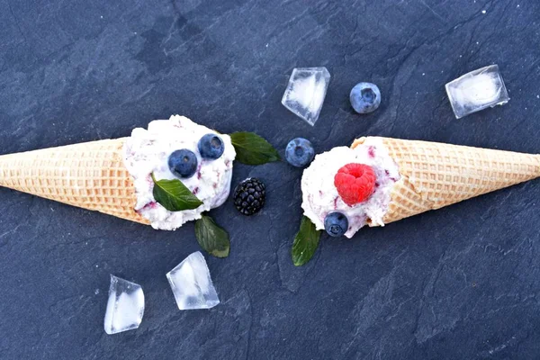 waffle ice cream cones filled with forest fruit ice cream balls with fresh berries and mint lying on a dark marble surface - concept for a cool summer adventure with delicious fruity ice cream