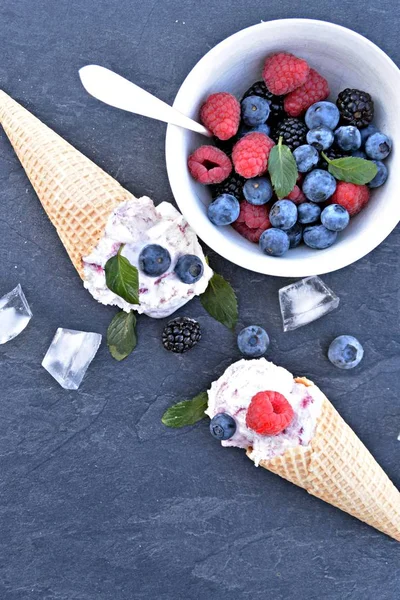 waffle ice cream cones filled with forest fruit ice cream balls with fresh berries and mint lying on a dark marble surface - concept for a cool summer adventure with delicious fruity ice cream