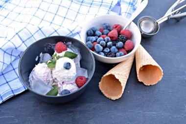 Koyu bir mutfak yüzeyinde yanında nane yaprakları ve dondurma waffle ile yabani berry dondurma topları dolu koyu bir kase - yaz için ferahlatıcı meyve buz ile kavram