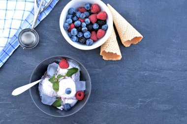 Koyu bir mutfak yüzeyinde yanında nane yaprakları ve dondurma waffle ile yabani berry dondurma topları dolu koyu bir kase - yaz için ferahlatıcı meyve buz ile kavram