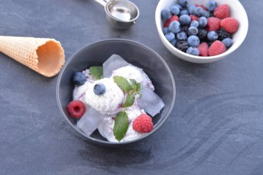 Koyu bir mutfak yüzeyinde yanında nane yaprakları ve dondurma waffle ile yabani berry dondurma topları dolu koyu bir kase - yaz için ferahlatıcı meyve buz ile kavram