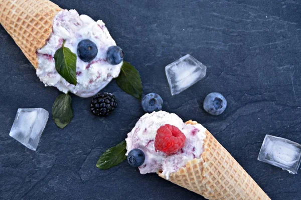 waffle ice cream cones filled with forest fruit ice cream balls with fresh berries and mint lying on a dark marble surface - concept for a cool summer adventure with delicious fruity ice cream