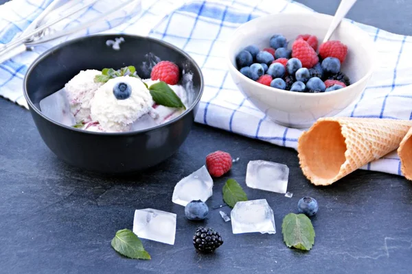 ミントの葉とアイスクリームワッフルが隣にダークキッチンの表面に野生のベリーアイスクリームボールでいっぱいのダークボウル 夏のためのさわやかなフルーツアイスとのコンセプト — ストック写真