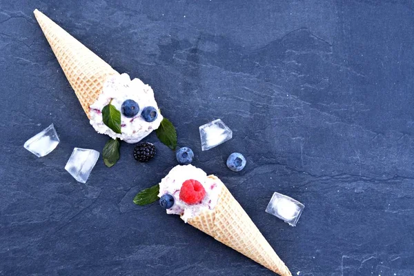 waffle ice cream cones filled with forest fruit ice cream balls with fresh berries and mint lying on a dark marble surface - concept for a cool summer adventure with delicious fruity ice cream