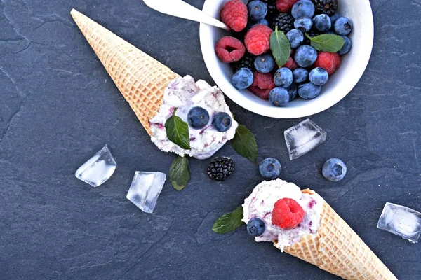 waffle ice cream cones filled with forest fruit ice cream balls with fresh berries and mint lying on a dark marble surface - concept for a cool summer adventure with delicious fruity ice cream