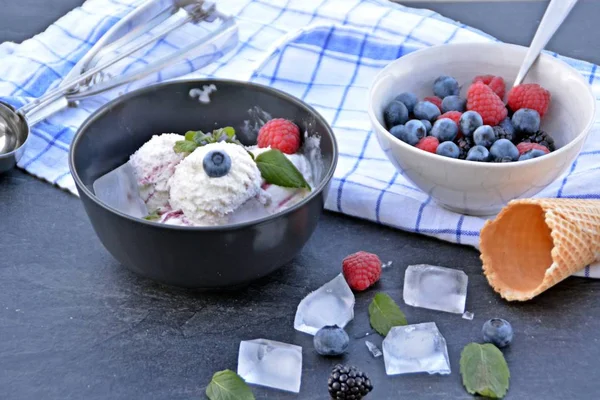 ミントの葉とアイスクリームワッフルが隣にダークキッチンの表面に野生のベリーアイスクリームボールでいっぱいのダークボウル 夏のためのさわやかなフルーツアイスとのコンセプト — ストック写真