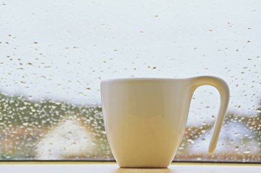 üzerinde su damlaları ile bir pencerenin önünde duran fincan