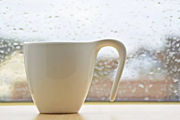 cup standing in front of a window with water drops on it