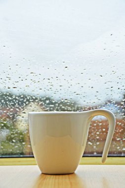 üzerinde su damlaları ile bir pencerenin önünde duran fincan