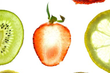 Portakal, çilek ve kivi gibi farklı dilimlenmiş meyveler parlak beyaz bir arka plan üzerinde yatıyor ve ışık ile yukarıdan aydınlatılır - farklı renklerde taze ve sağlıklı meyve kavramı - 