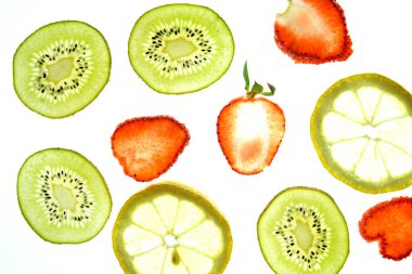 Portakal, çilek ve kivi gibi farklı dilimlenmiş meyveler parlak beyaz bir arka plan üzerinde yatıyor ve ışık ile yukarıdan aydınlatılır - farklı renklerde taze ve sağlıklı meyve kavramı - 